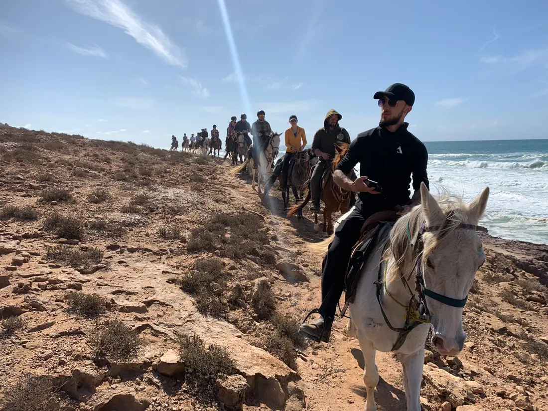 A line of riders on horseback along a cliff-top path above the Atlantic surf