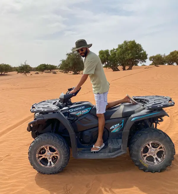 A quad bike parked on orange dunes with argan trees behind